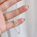 Hand holding gold plated necklace with oval pendant and sparkling stones, minimalist jewelry