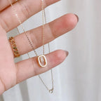 Hand holding gold plated necklace with oval pendant and sparkling stones, minimalist jewelry