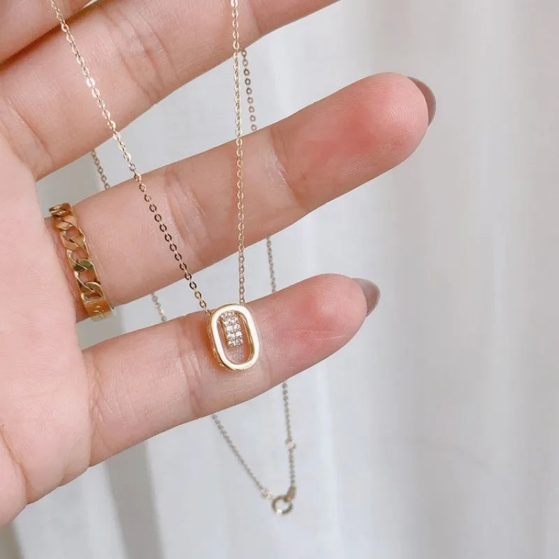 Hand holding gold plated necklace with oval pendant and sparkling stones, minimalist jewelry