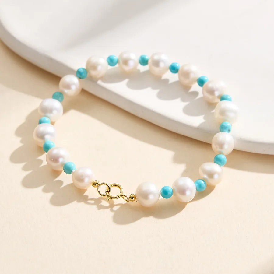 Gold clasp bracelet with round white pearls and turquoise beads on a light background