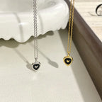Gold and silver heart pendant necklaces with black enamel on a white textured surface