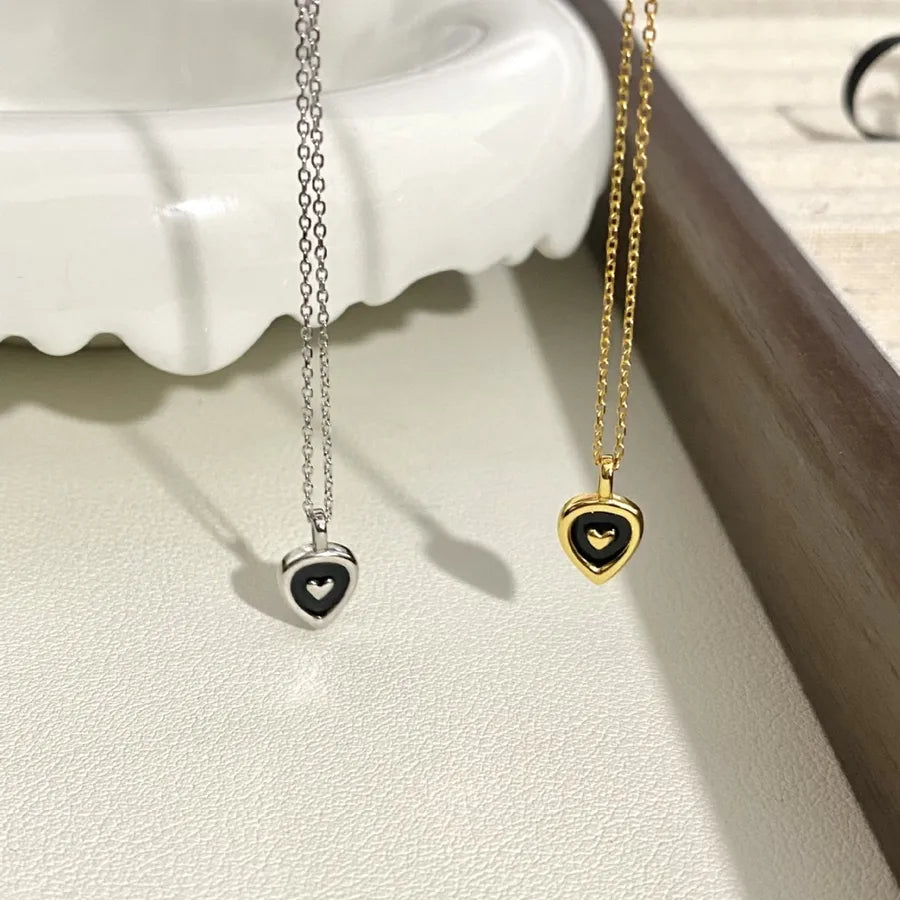 Gold and silver heart pendant necklaces with black enamel on a white textured surface