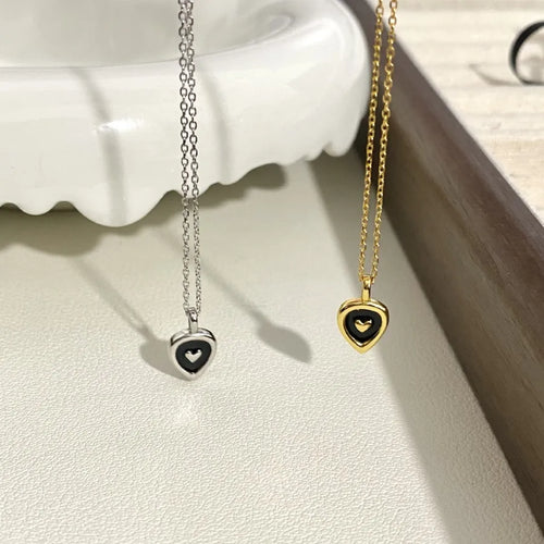Gold and silver heart pendant necklaces with black enamel on a white textured surface