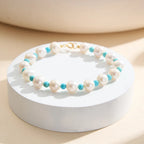 Pearl and turquoise beaded bracelet with gold clasp on a white display stand