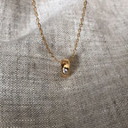 18K gold plated pendant necklace with single clear stone on textured fabric background