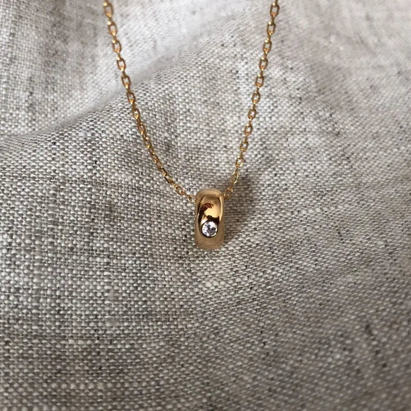 18K gold plated pendant necklace with single clear stone on textured fabric background