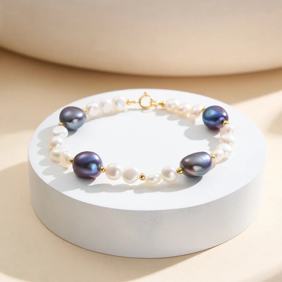 Gold clasp bracelet with white and purple freshwater pearls on round display stand