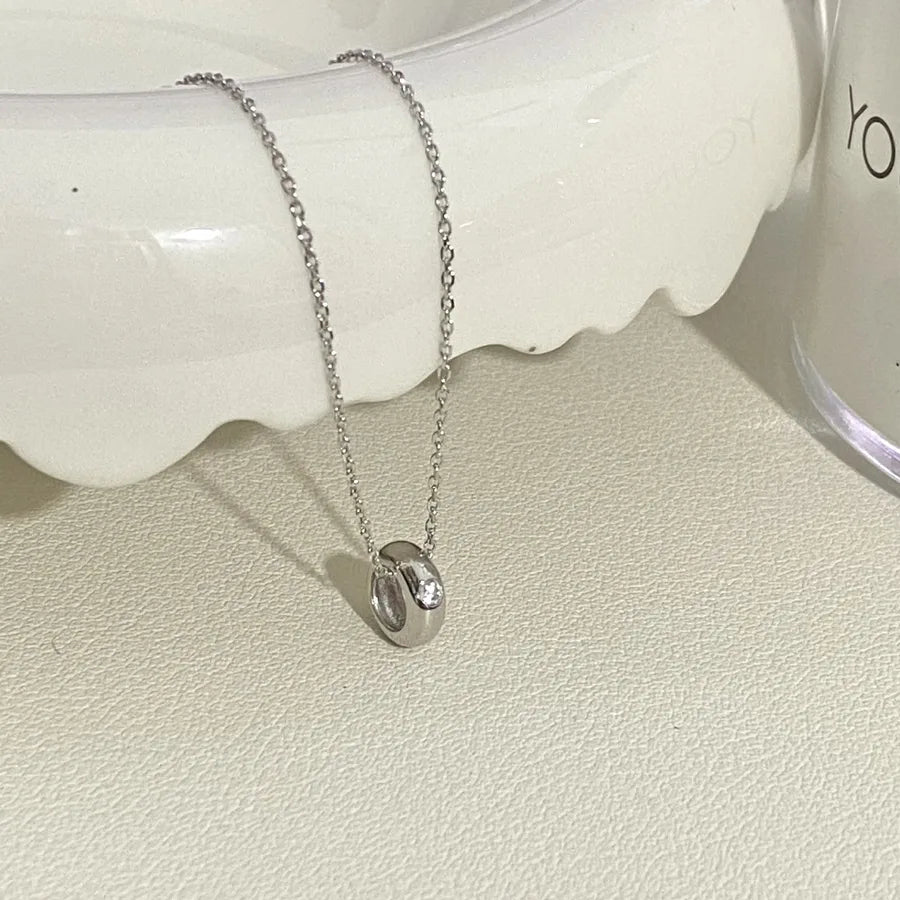 Silver chain necklace with minimalist round pendant and clear stone on a cream background