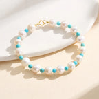 Pearl and turquoise beaded bracelet with gold clasp on neutral background