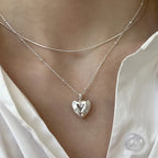 Layered silver necklaces with a heart-shaped pendant worn over a white blouse