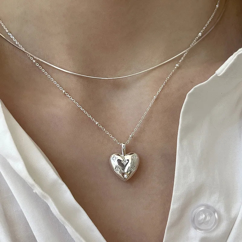 Layered silver necklaces with a heart-shaped pendant worn over a white blouse