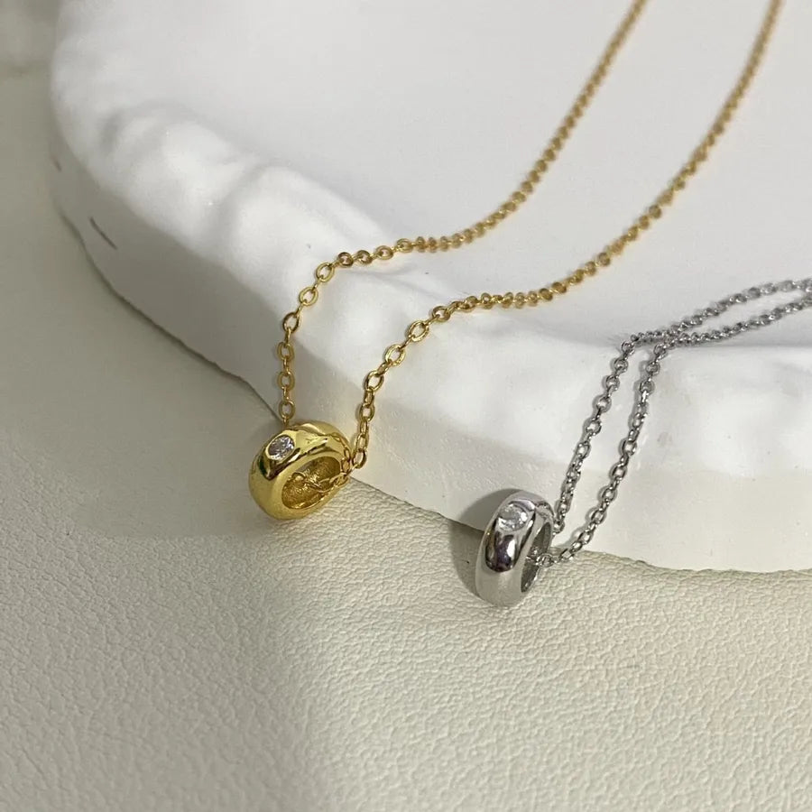 Gold and silver pendant necklaces with round charms and clear stones on a textured surface