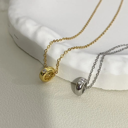 Gold and silver pendant necklaces with round charms and clear stones on a textured surface