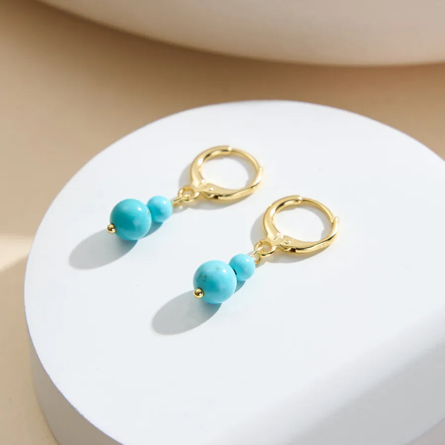 Gold hoop earrings with turquoise beads on a white display, demi-fine jewelry