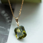 Gold chain necklace with emerald-cut green gemstone pendant, elegant jewelry closeup