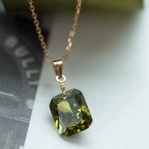 Gold chain necklace with emerald-cut green gemstone pendant, elegant jewelry closeup