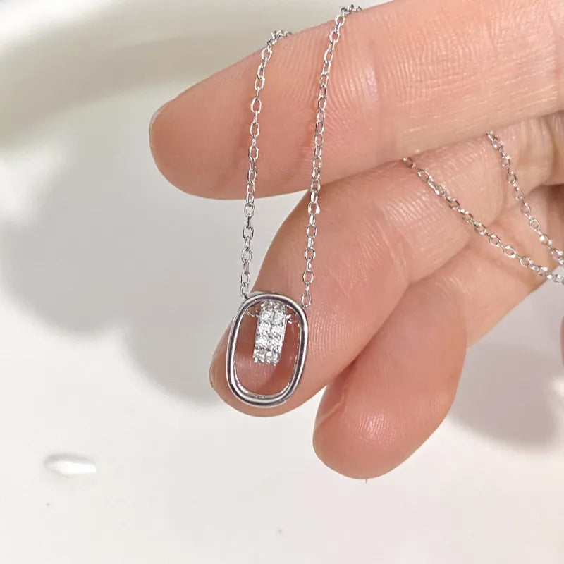 Silver oval pendant necklace with cubic zirconia, delicate chain, held between fingers