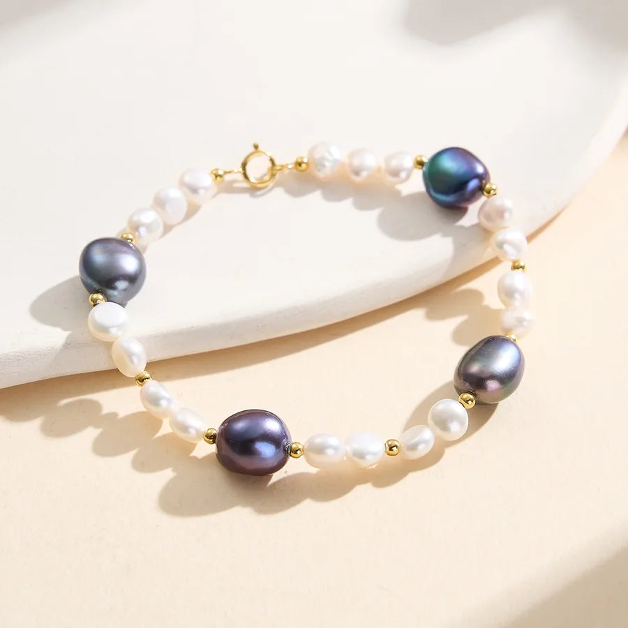 Gold-plated bracelet with white and black freshwater pearls on a neutral background