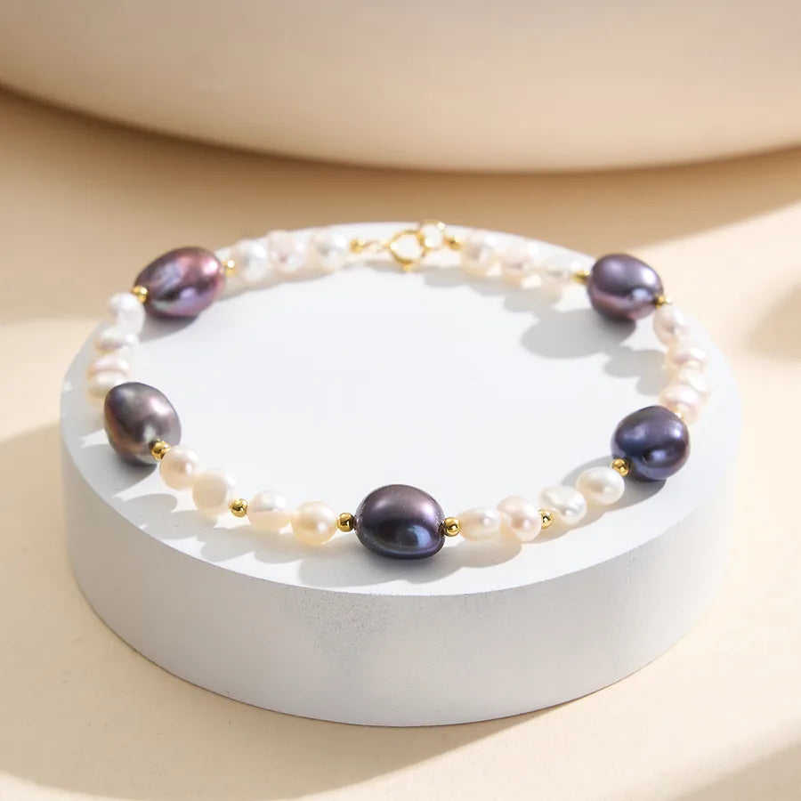Bracelet with white freshwater pearls, black pearls, and gold bead accents on display.
