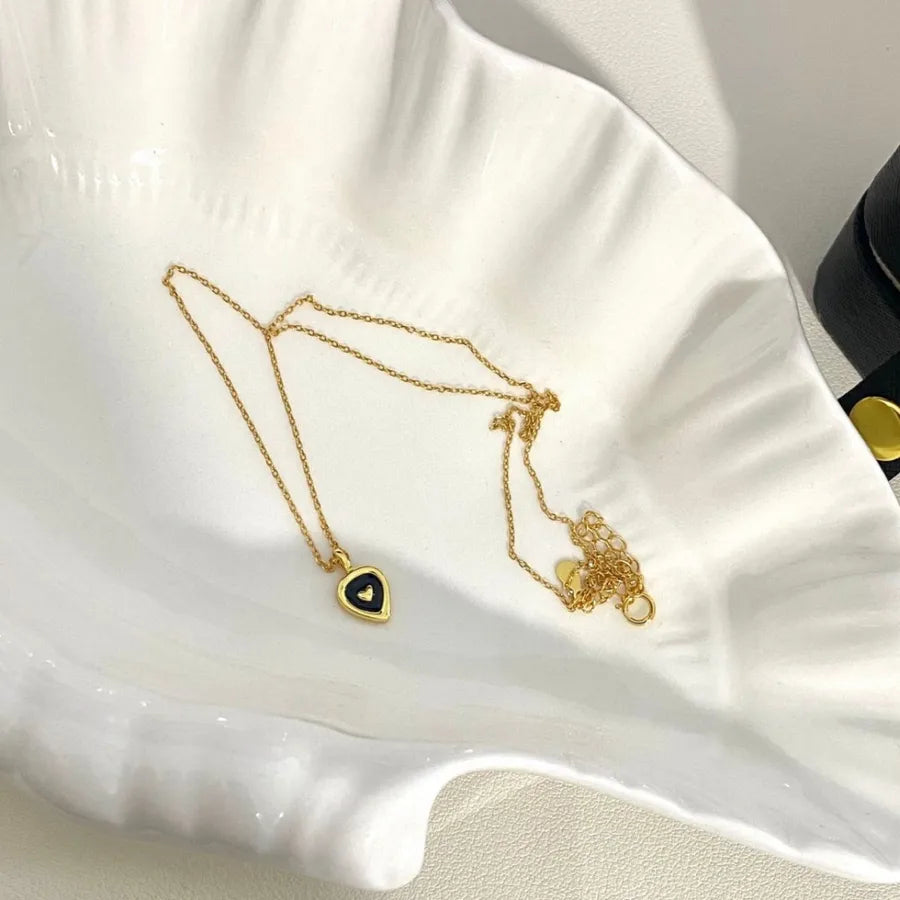 Gold heart pendant necklace with black center on a scalloped white dish