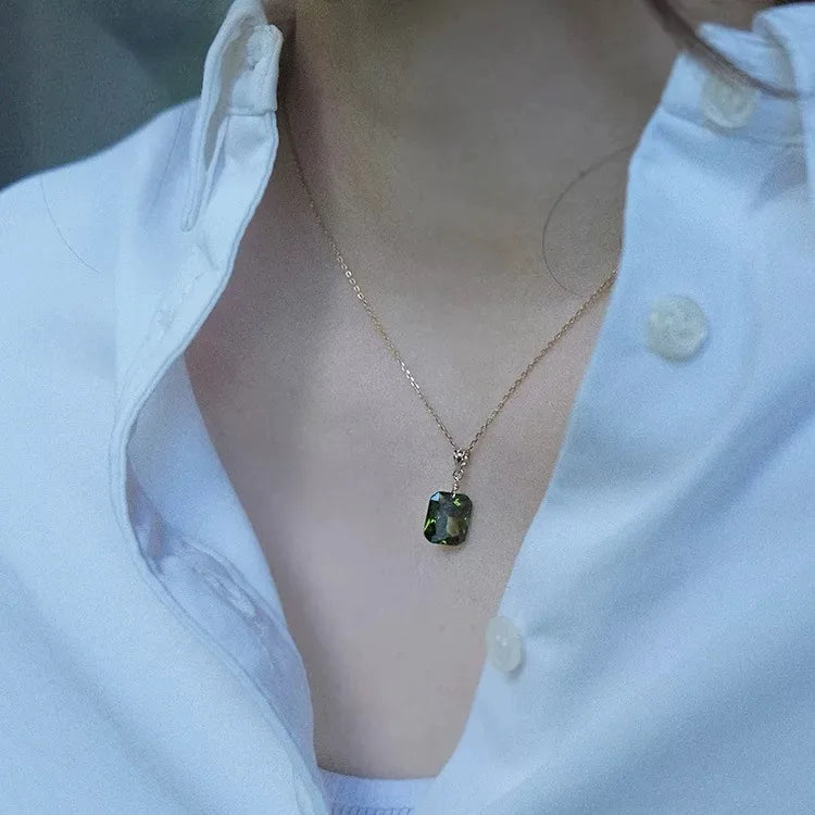18K gold plated chain necklace with green gemstone pendant worn over a white shirt