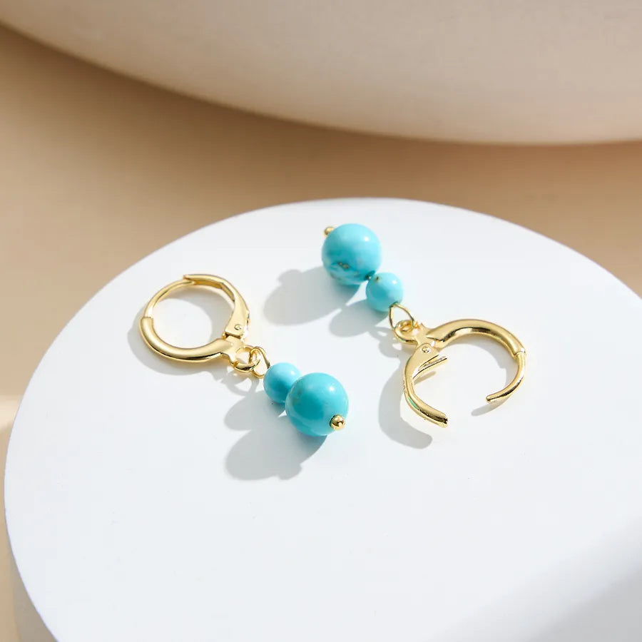 Gold hoop earrings with turquoise beads, demi-fine jewelry on white display