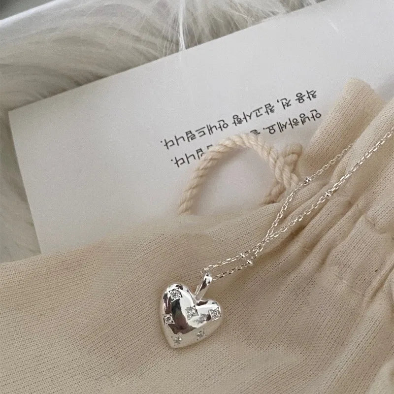Silver heart pendant necklace with star accents on a beige fabric pouch, elegant jewelry.