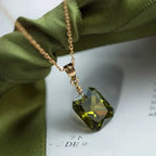Gold chain necklace with green emerald-cut gemstone pendant on fabric background