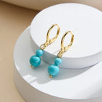 Gold leverback earrings with double turquoise beads on a white display, demi-fine jewelry