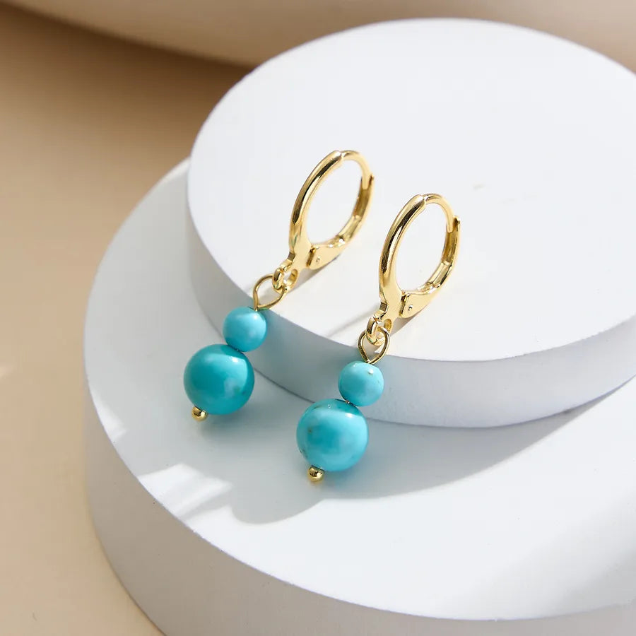 Gold leverback earrings with double turquoise beads on a white display, demi-fine jewelry